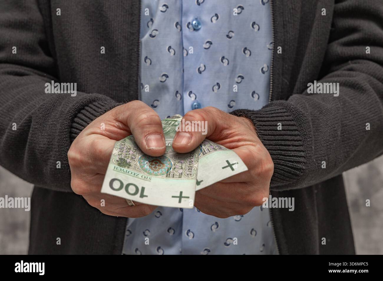 Un uomo con una camicia blu e un maglione tiene i soldi in mano, contando i soldi prima di spenderli. Foto Stock