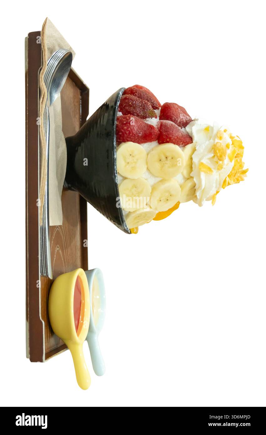 Un set di Bingsu coreano in una piccola ciotola nera con diversi condimenti di frutta e salsa rossa con latte condensato dolce in mini ciotole di plastica in legno marrone Foto Stock
