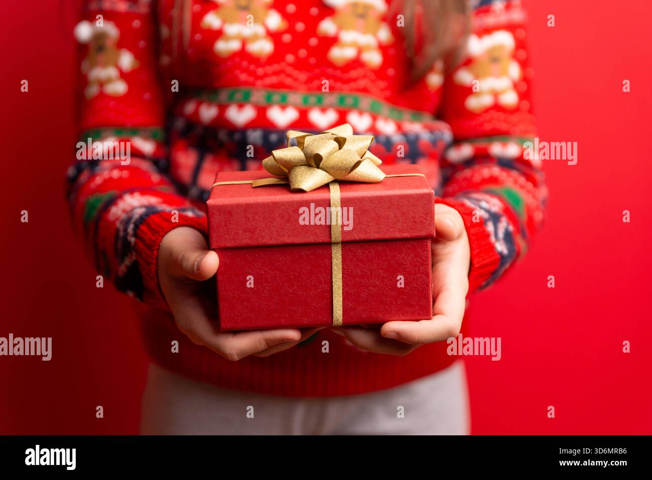 Bambino con in mano una confezione regalo rossa con fiocco dorato su sfondo rosso brillante, perfetta per temi natalizi, marketing natalizio e grafica stagionale Foto Stock