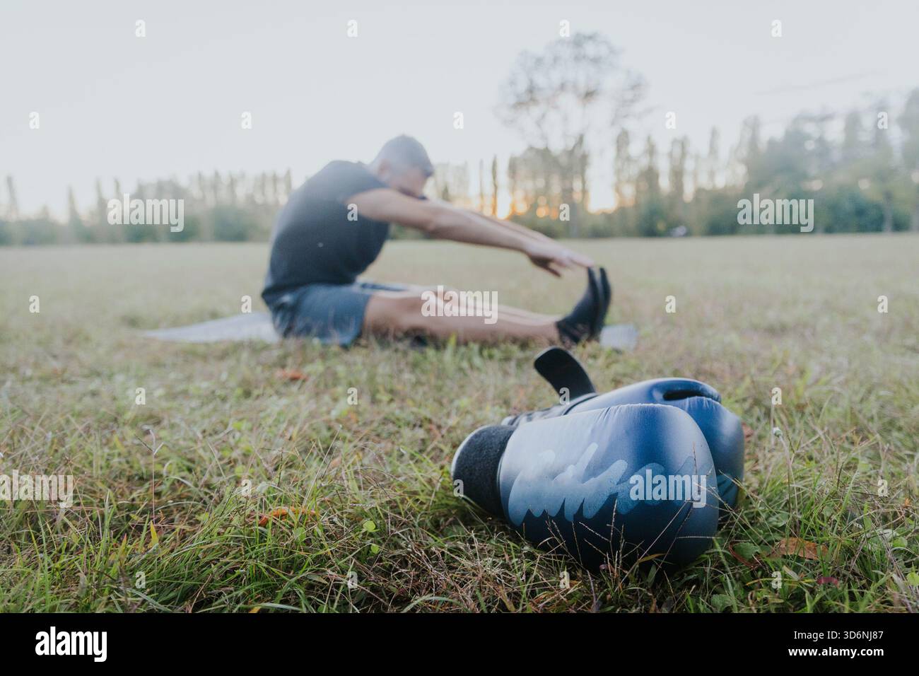 Guanti da boxe riposati sull'erba mentre l'uomo si allunga prima di allenarsi in un parco all'aperto. Foto Stock
