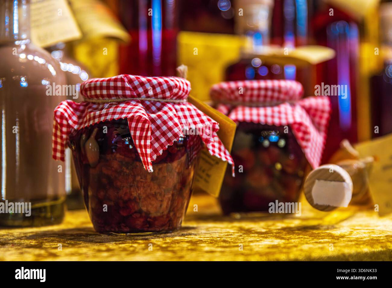 Marmellata rustica fatta in casa in mostra durante le feste. Un primo piano di vasetti di marmellata artigianali con coperchi rossi di Vichy disposti su una tovaglia dorata in un tradizionale holid Foto Stock