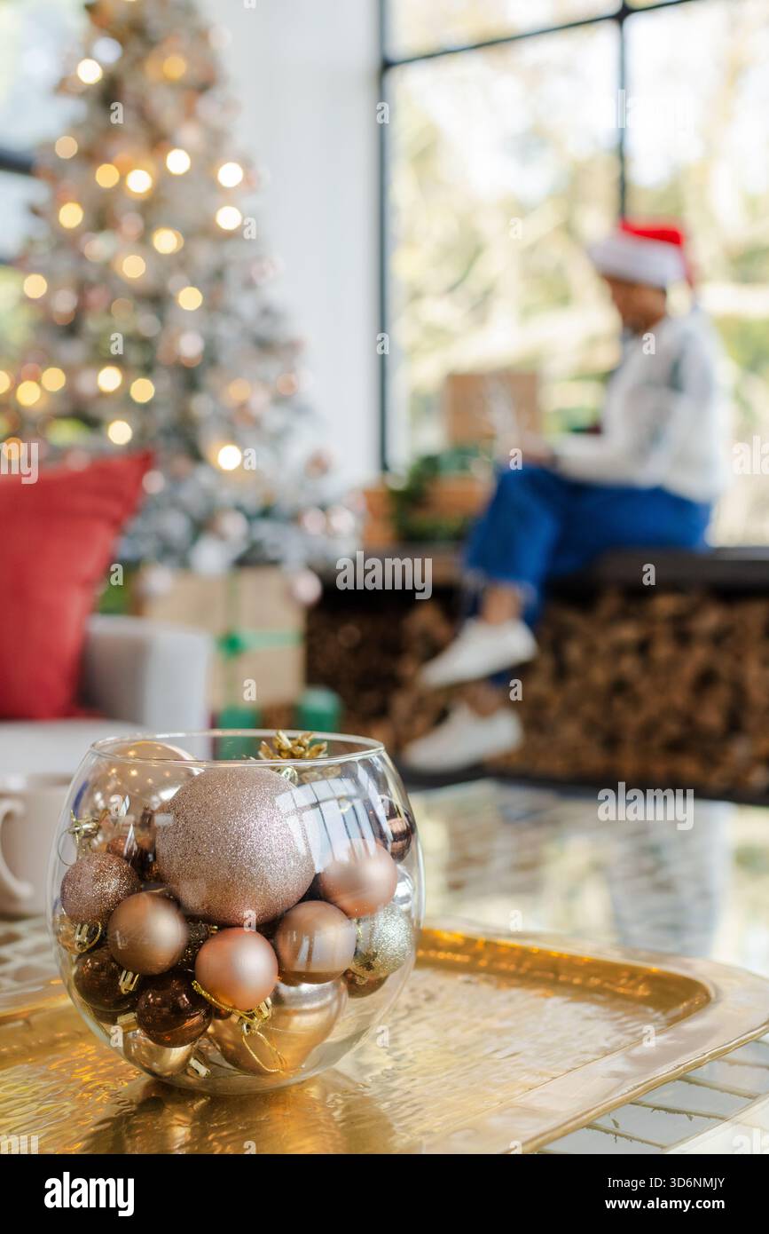 Ciotola con baule sul vassoio, albero luminoso accanto ai regali, portatore di Babbo Natale che usa il dispositivo Foto Stock