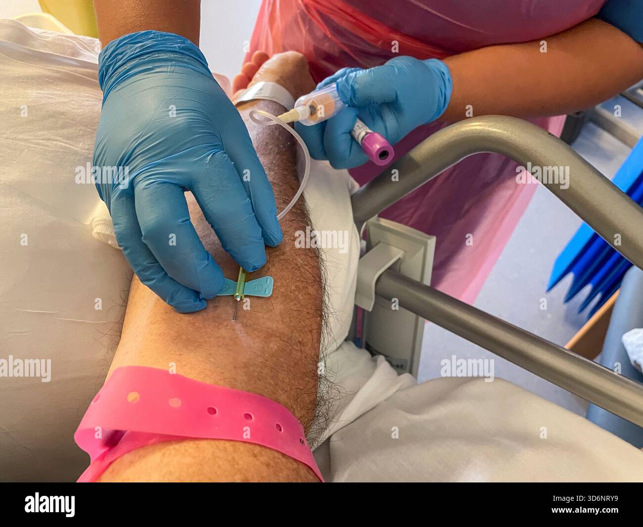 Operatore sanitario che inserisce una cannula nel braccio di un paziente maschio adulto per prelevare un campione di sangue in un ambiente clinico: Phillip Roberts - Immagine stock catturata con smartphone