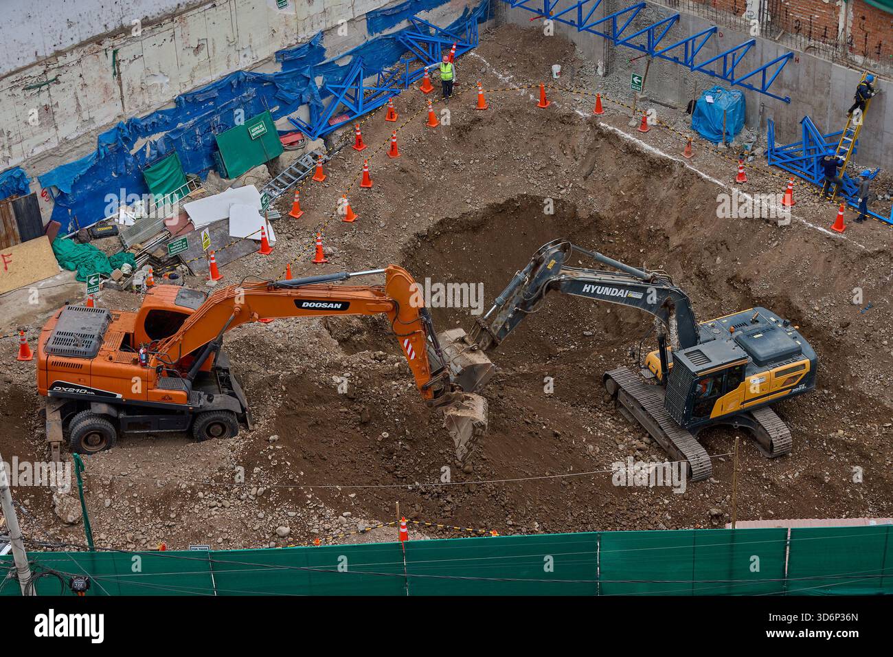 Due escavatori scavano tra strati di terreno e roccia, coordinando i loro movimenti per preparare la base di un progetto di costruzione attivo. Foto Stock