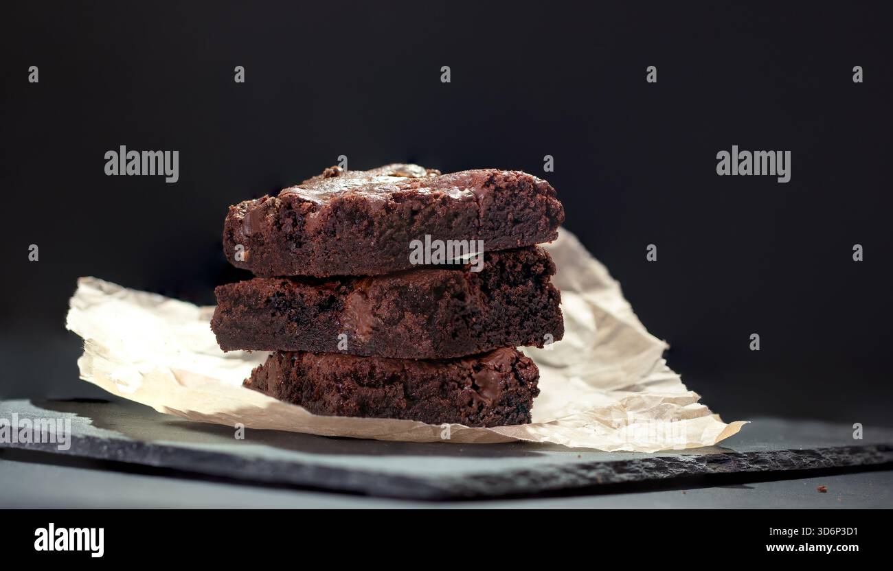 Una pila di deliziosi brownie al cioccolato su sfondo scuro Foto Stock