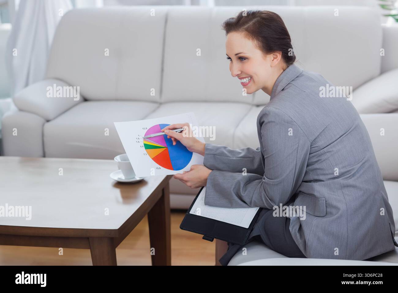 Donna in blazer seduto sul divano in salotto con un grafico a torta che punta con penna e spazio copia. Executive, portfolio, report, presentazione, analisi, corp Foto Stock