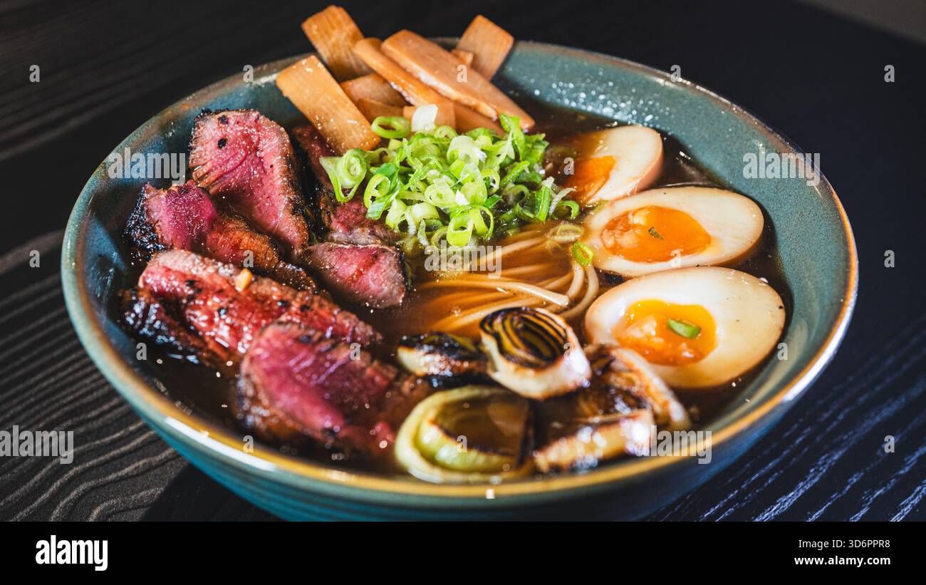 Ramen di manzo salato con rare fette di bistecca, cipollotti, germogli di bambù, porri e uova tamago. Brodo ricco, sapori autentici, perfetto per il cu giapponese Foto Stock
