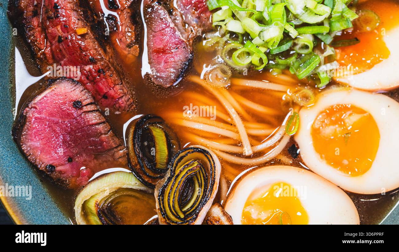 Ramen di manzo salato con rare fette di bistecca, cipollotti, germogli di bambù, porri e uova tamago. Brodo ricco, sapori autentici, perfetto per il cu giapponese Foto Stock