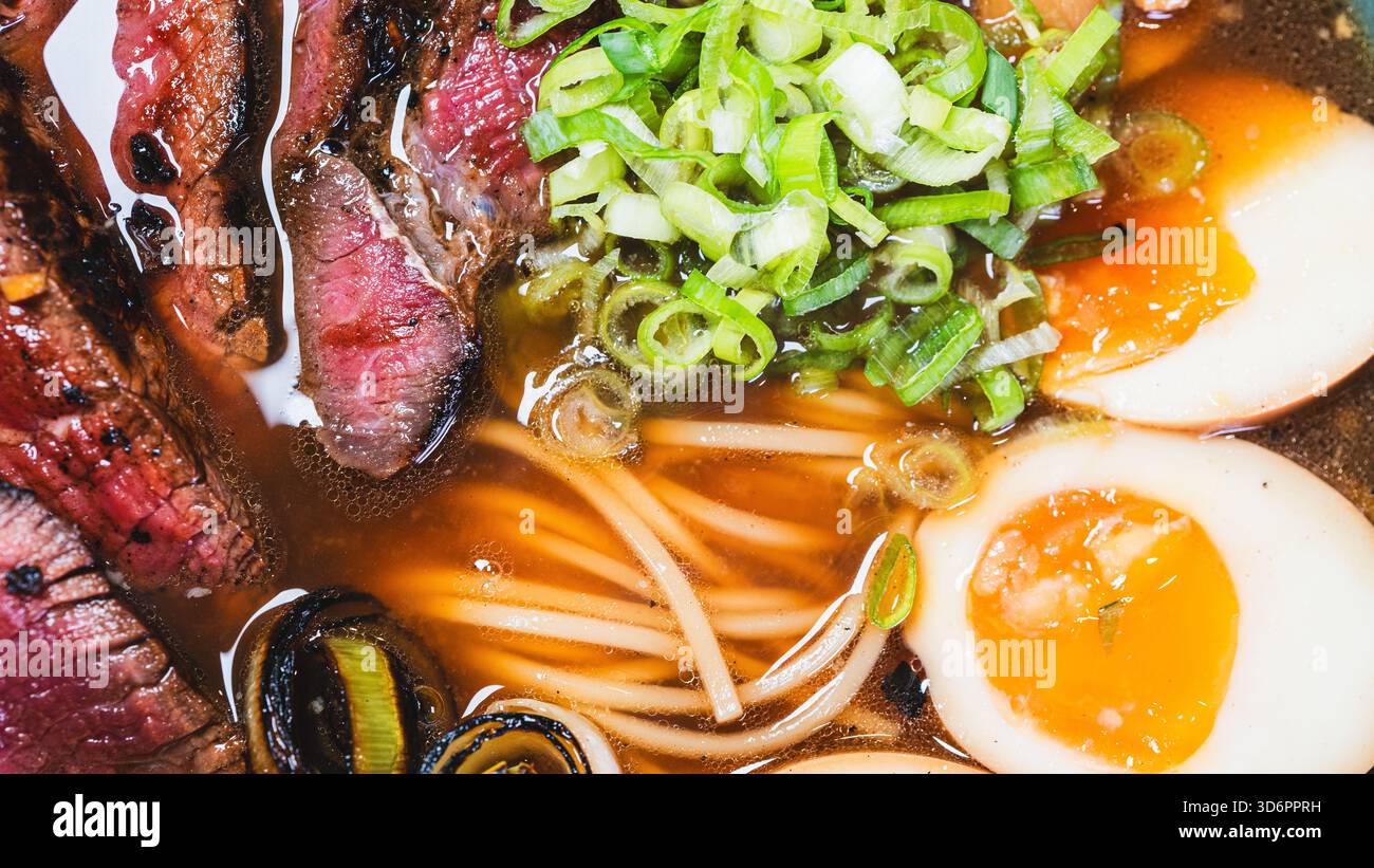 Ramen di manzo salato con rare fette di bistecca, cipollotti, germogli di bambù, porri e uova tamago. Brodo ricco, sapori autentici, perfetto per il cu giapponese Foto Stock