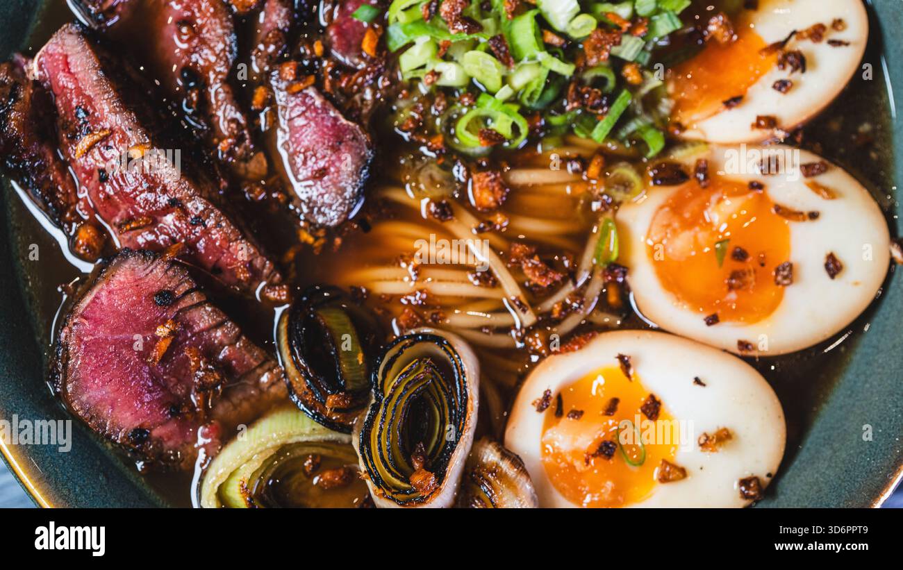 Ramen di manzo salato con rare fette di bistecca, cipollotti, germogli di bambù, porri e uova tamago. Brodo ricco, sapori autentici, perfetto per il cu giapponese Foto Stock