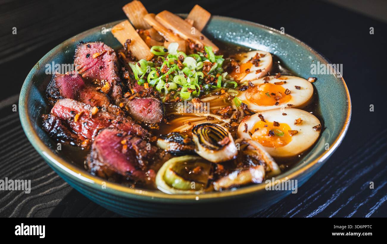 Ramen di manzo salato con rare fette di bistecca, cipollotti, germogli di bambù, porri e uova tamago. Brodo ricco, sapori autentici, perfetto per il cu giapponese Foto Stock