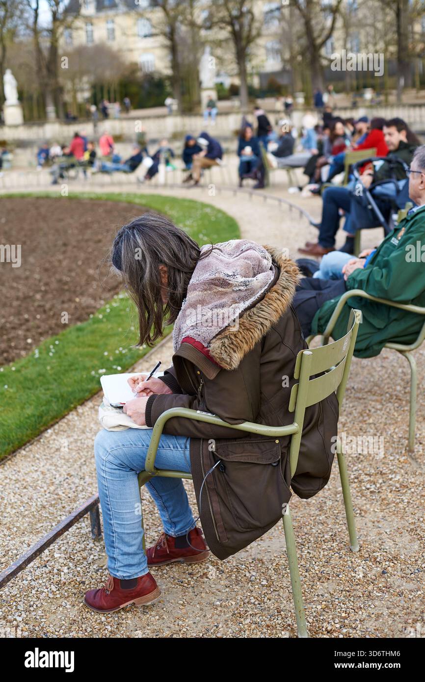Parigi, Francia - marzo 2025: I visitatori si rilassano sotto gli alberi nel Jardin du Luxembourg, uno splendido parco di Parigi. Una persona siede su una sedia verde, drawi Foto Stock