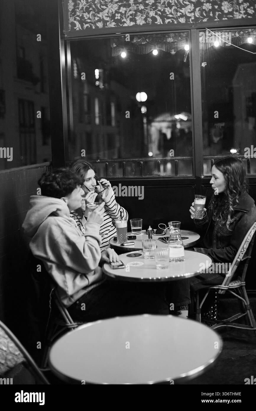 Amici che sorseggiano un drink in un accogliente caffè a Montmartre, Parigi di notte, Parigi, Francia Foto Stock