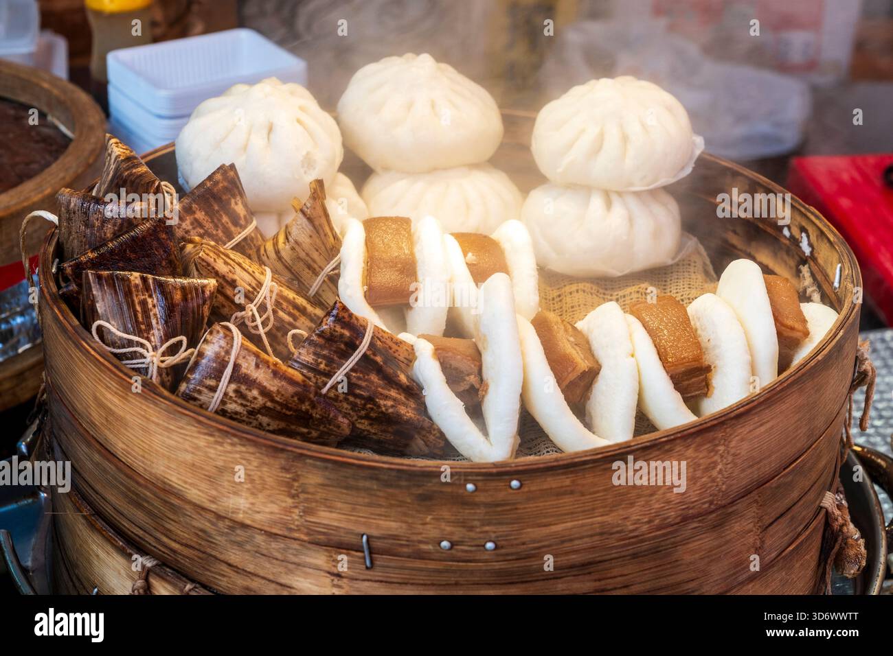 Primo piano di gnocchi cinesi e panini di maiale cotti in una ciotola di bambù su una bancarella di cibo da asporto caldo nel popolare quartiere di Chinatown. Foto Stock