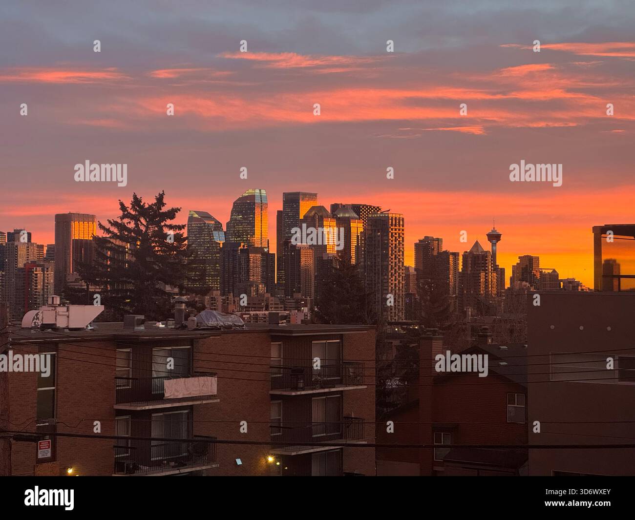 Caldo tramonto arancione e rosa sul centro di Calgary con grattacieli scintillanti ed edifici residenziali in primo piano. - Immagine stock catturata con smartphone