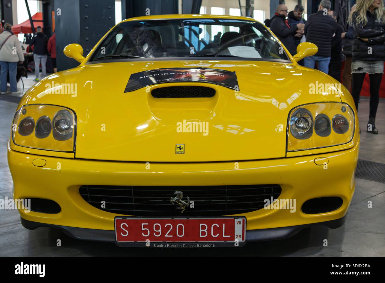 Vista frontale di un'iconica auto sportiva gialla di lusso che riflette la luce in una mostra automobilistica, attirando l'attenzione del pubblico Foto Stock