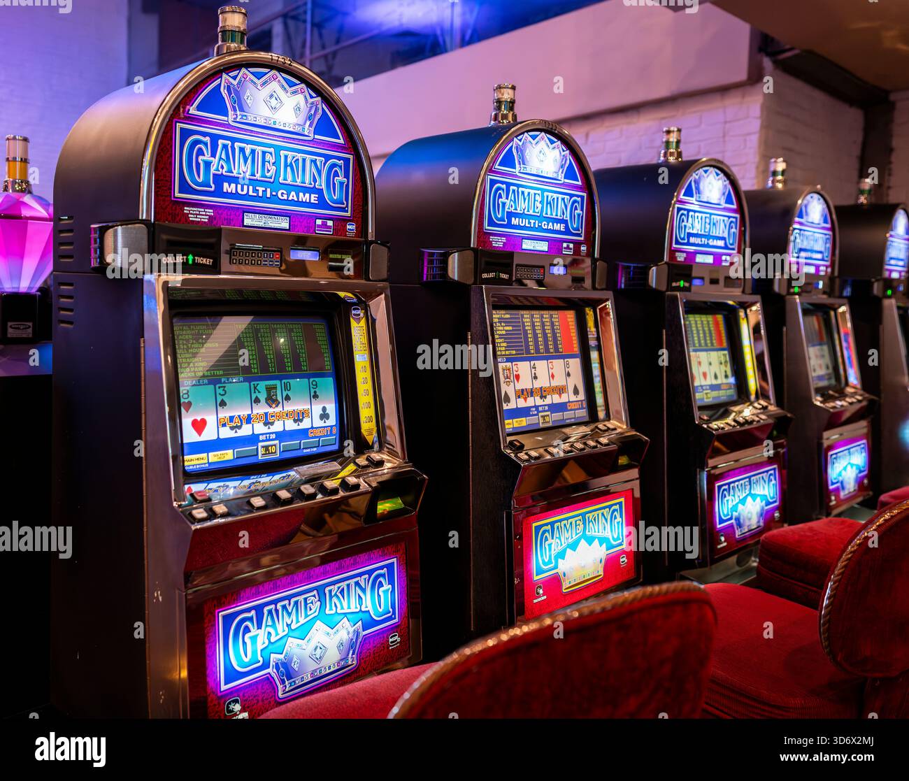 Videopoker Row of Game King all'interno di un casinò, con schermi illuminati, simboli di carte, posti a sedere rossi e un ambiente di gioco classico. Foto Stock