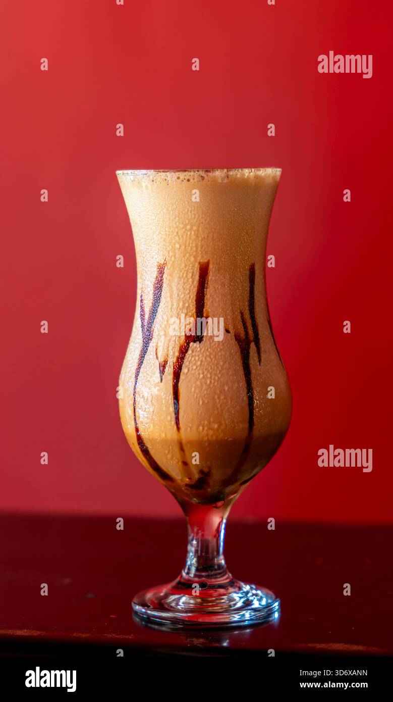 Cocktail di algarrobina peruviana a base di pisco servito in un bicchiere freddo su un vivace sfondo rosso, che mostra una ricca consistenza cremosa. Foto Stock