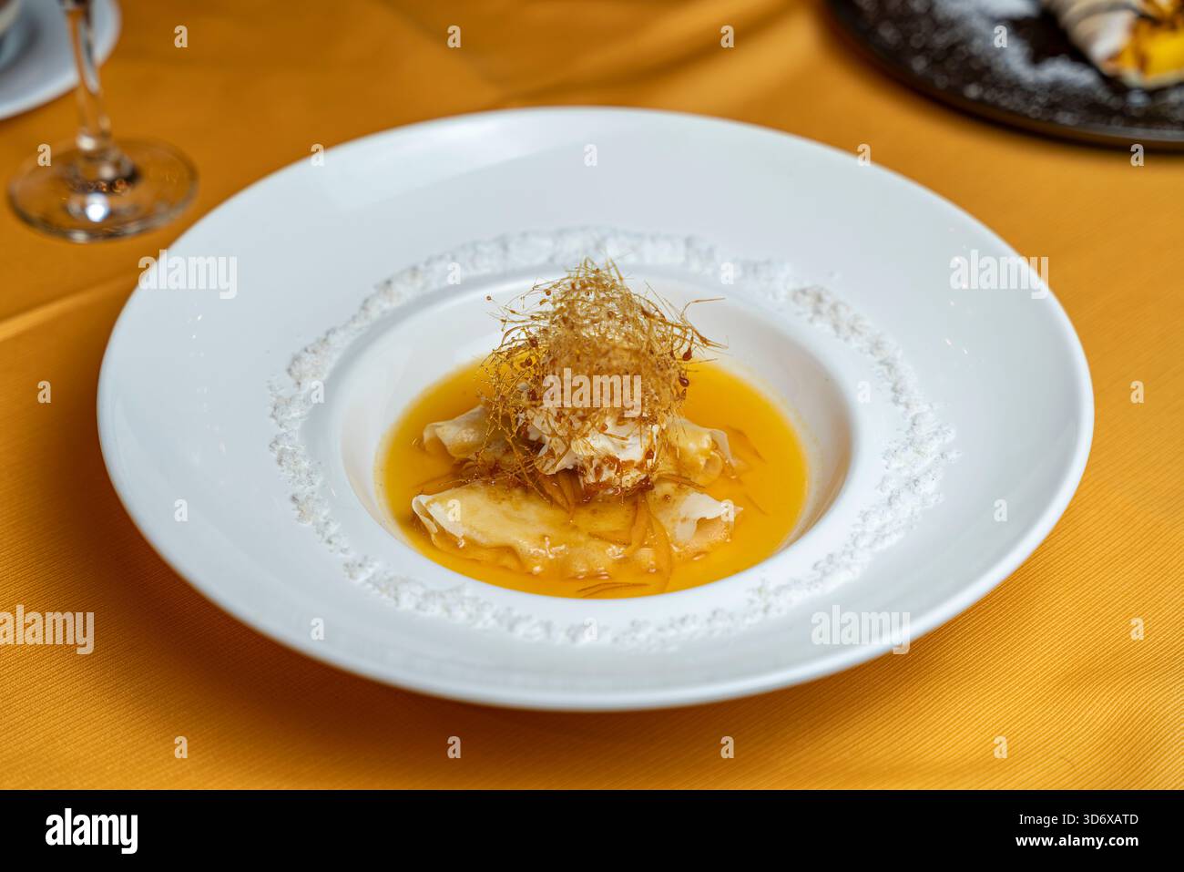 Crepes Suzette servite con salsa d'arancia brillante e fili di caramello su un piatto bianco in un ambiente ristorante con elegante presentazione gourmet. Foto Stock