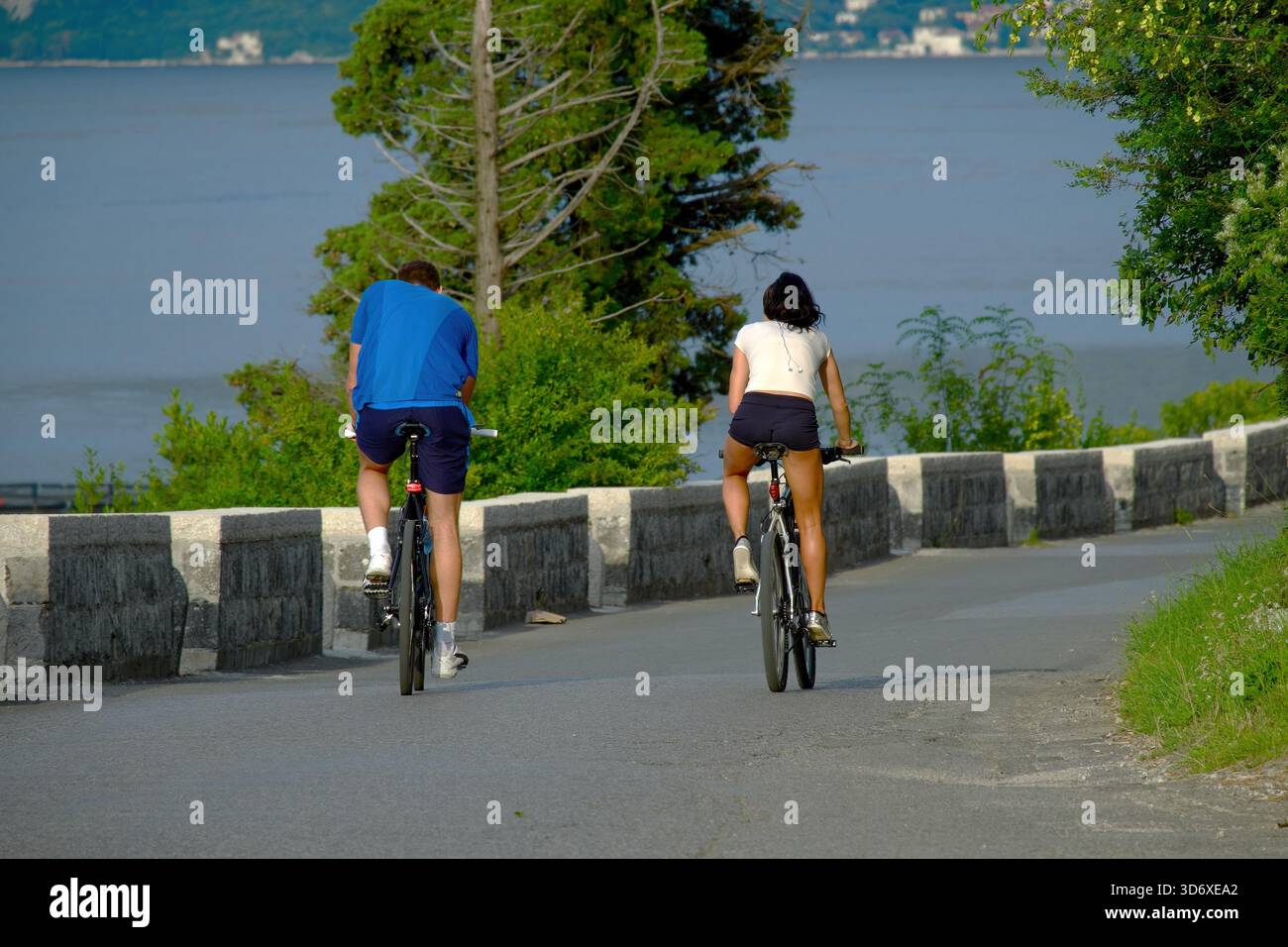 Uomo e donna in bicicletta sulla strada lungo la Baia di Cattaro, Montenegro Foto Stock