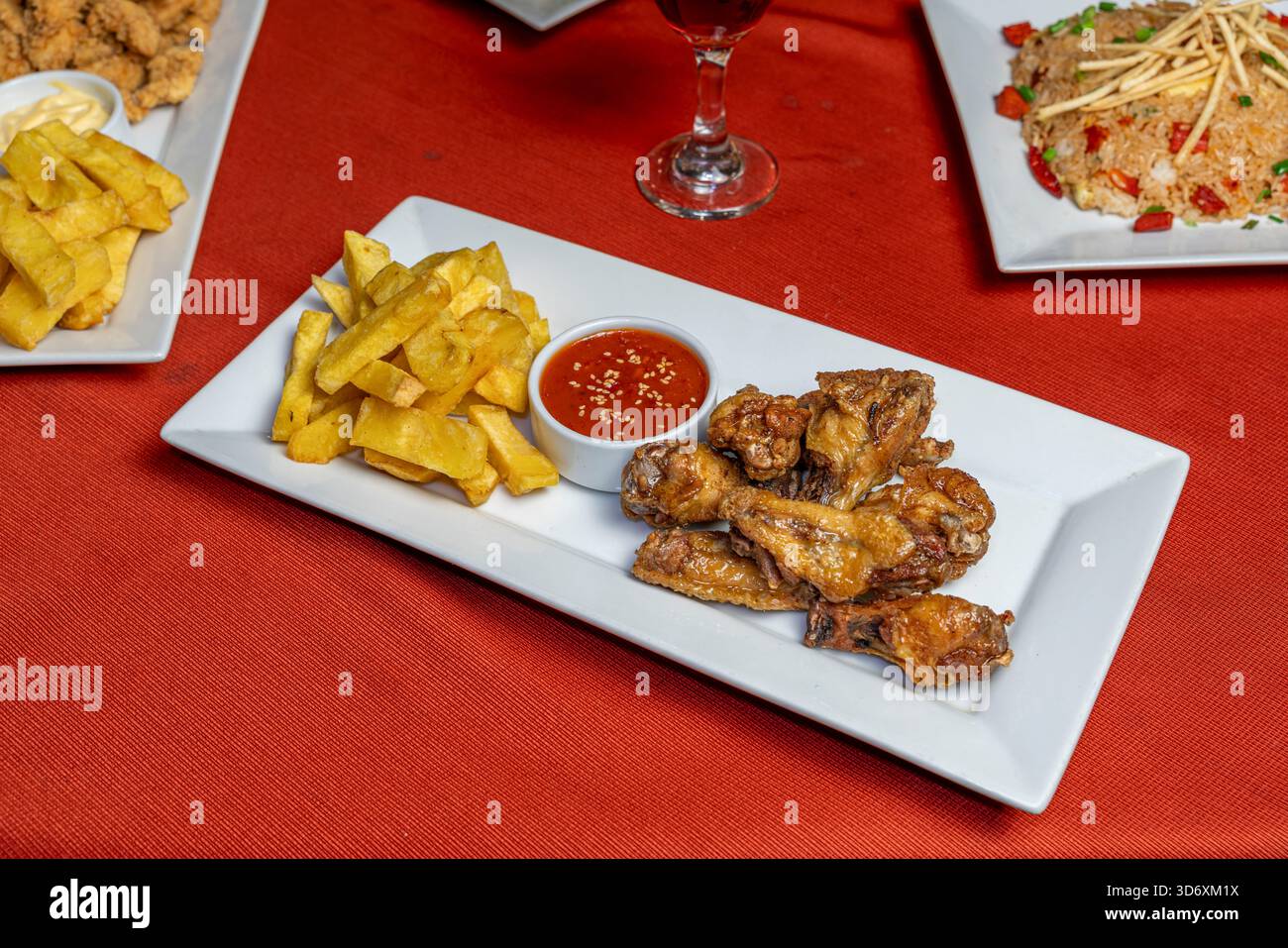 Ali di pollo fritte croccanti con patatine fritte e salsa piccante su un piatto bianco per promozioni culinarie. Foto Stock