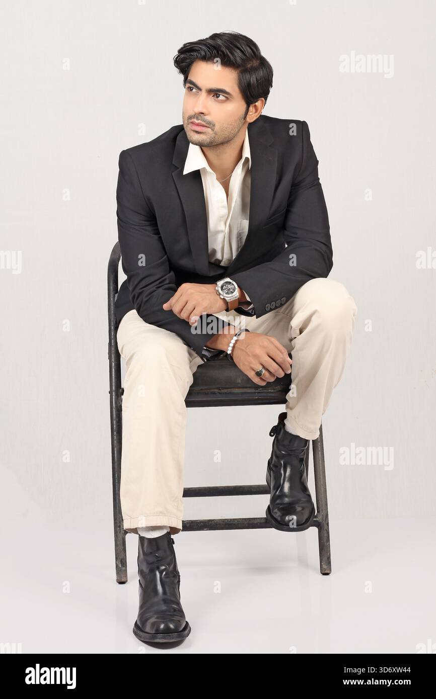 Ritratto di un giovane e alla moda barba in blazer nero con stile su sfondo bianco a tutta lunghezza e seduto sulla sedia Foto Stock