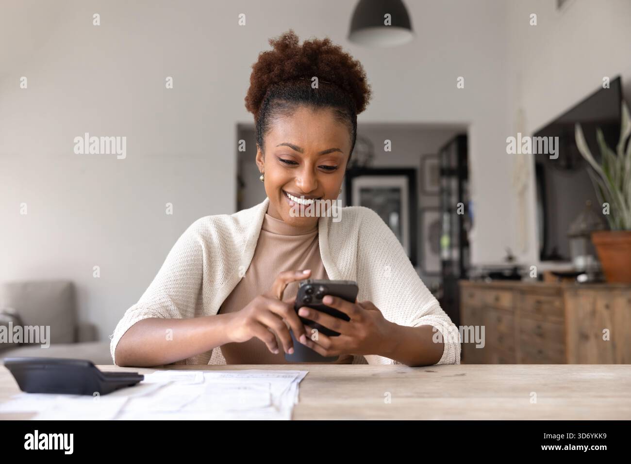 Felice giovane donna nera che scrive sul cellulare a tavola Foto Stock