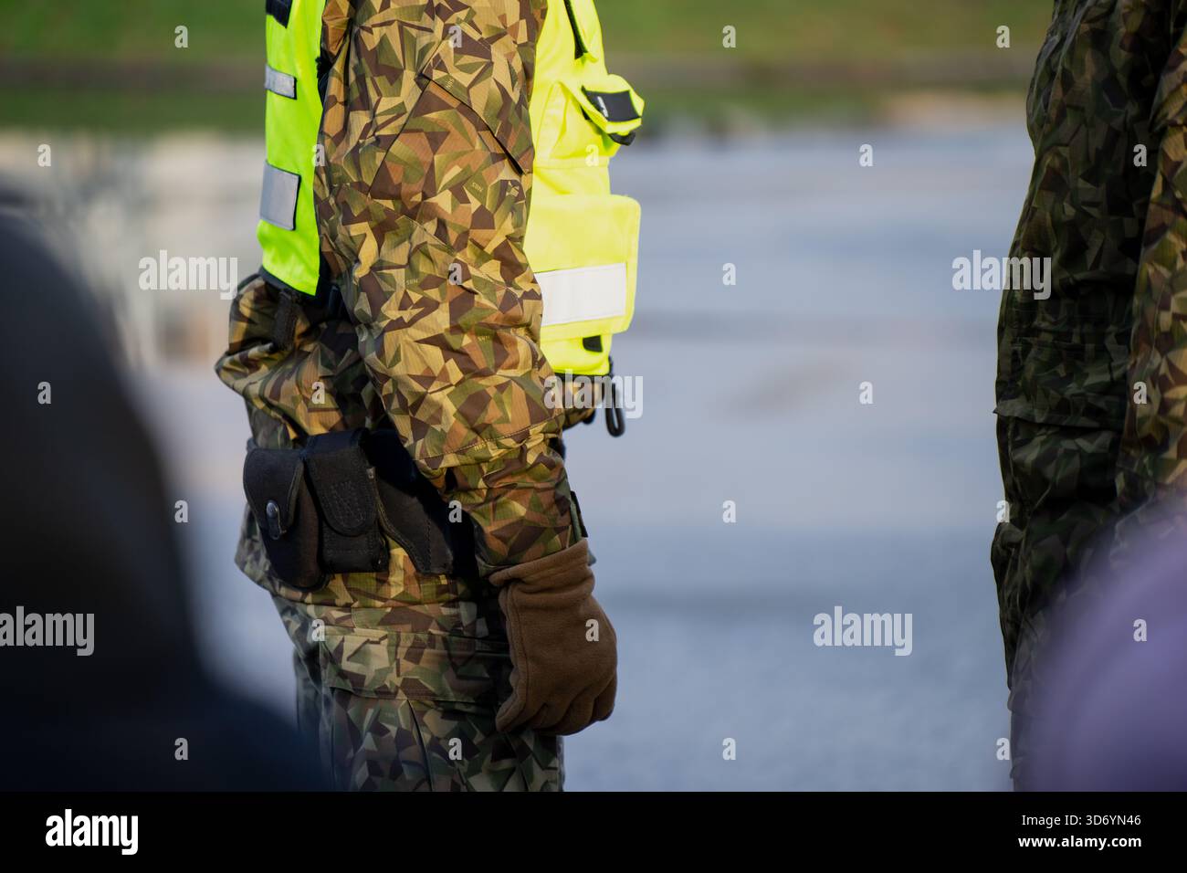 Personale militare che indossa uniforme mimetica, giubbotto ad alta visibilità e attrezzature tattiche in piedi all'aperto durante l'attività operativa, evidenziando Foto Stock