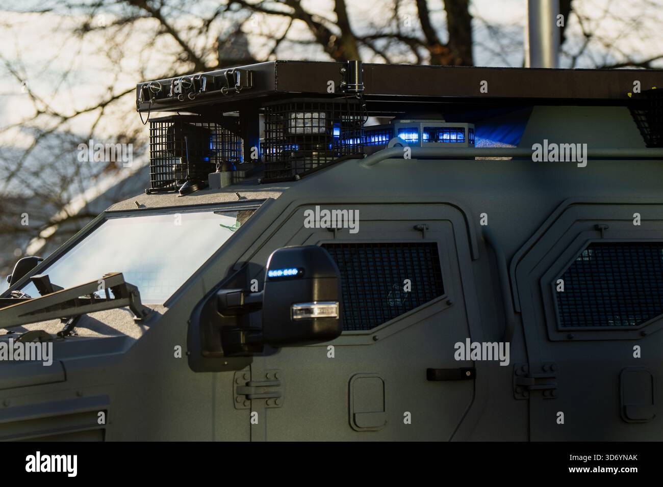 Veicolo tattico blindato con finestre a rete protettiva, sistema di copertura del tetto e luci di emergenza blu catturate alla luce del sole che mostrano pannelli rinforzati e Foto Stock