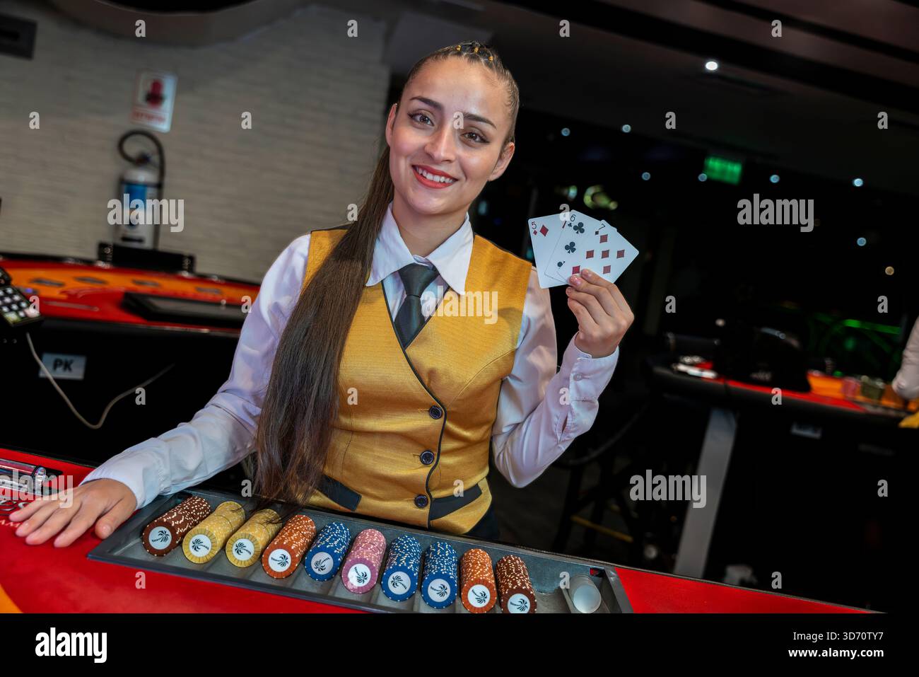 Mazziere di casinò donna che tiene carte da gioco dietro il tavolo da poker, servizio professionale, scenografia interna di lusso della sala da gioco Foto Stock