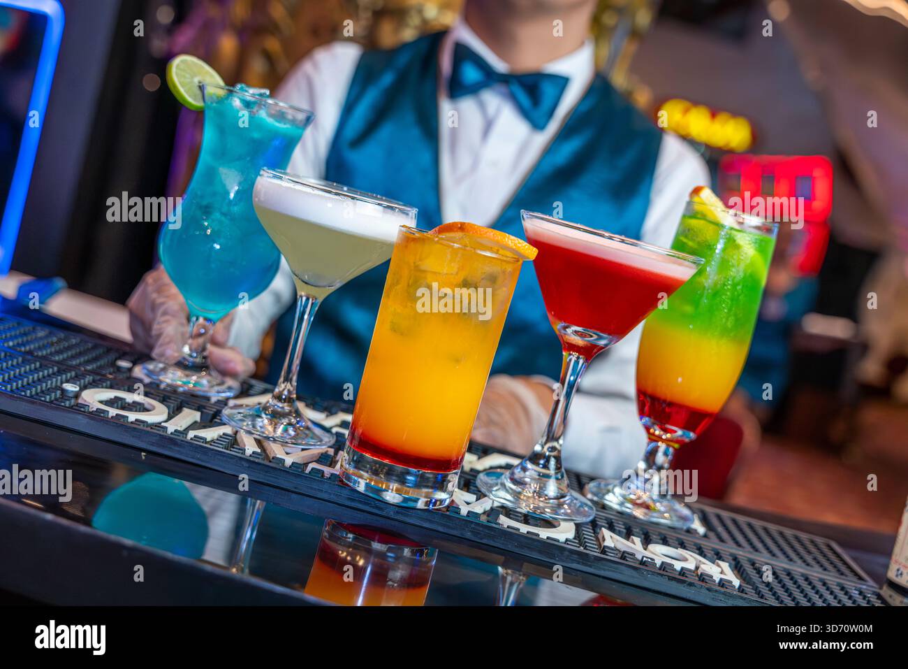 Cocktail colorati serviti da un barista in un bar del casinò con luci al neon, atmosfera notturna, bevande di lusso e intrattenimento. Foto Stock