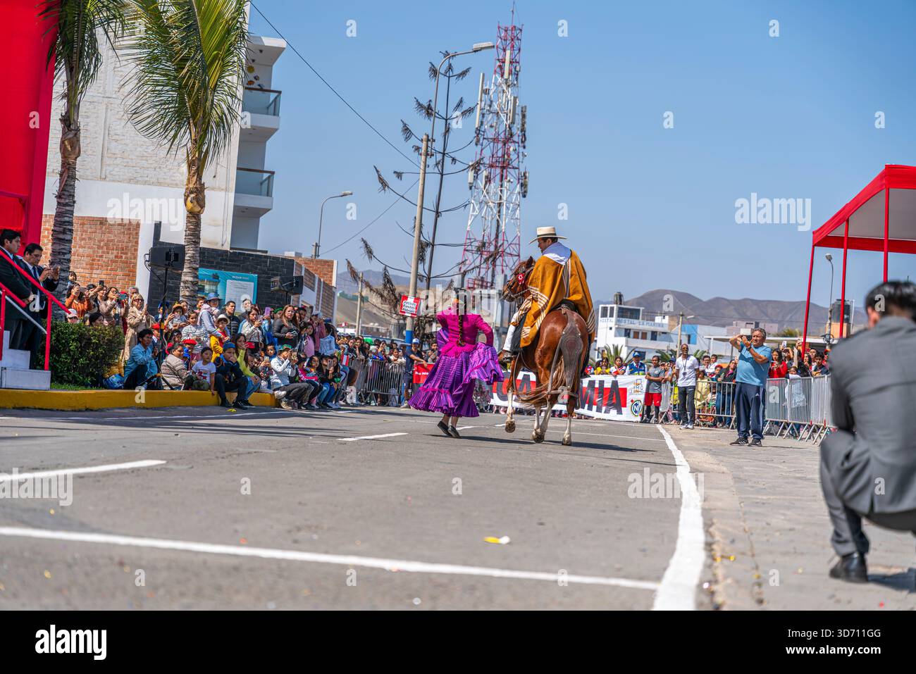I ballerini di Marinera si esibiscono durante una sfilata civica con cavalieri a cavallo mentre gli spettatori guardano lungo una strada urbana in Perù Foto Stock