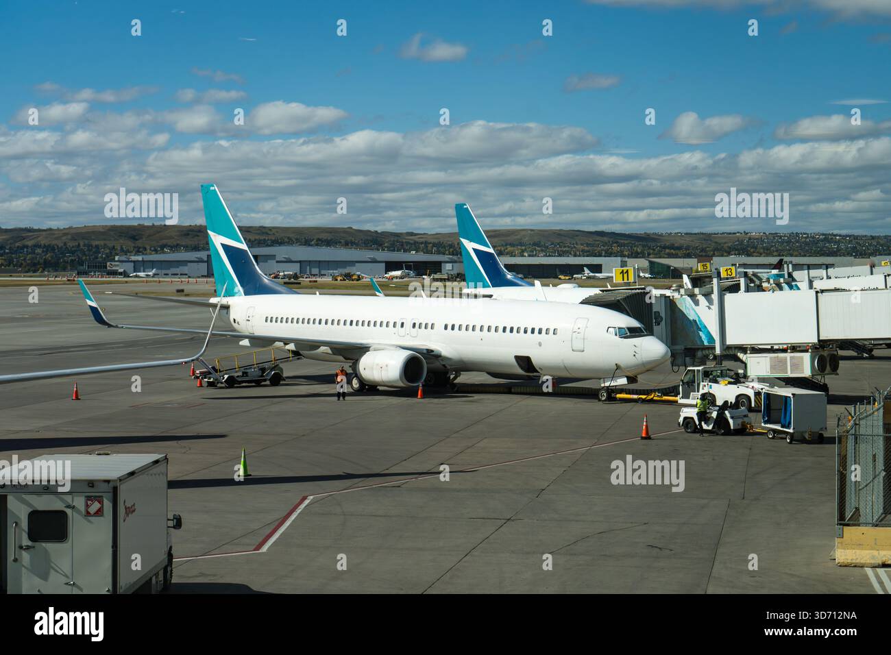 Due aerei parcheggiati sull'asfalto con un cielo nuvoloso e blu sullo sfondo. Aeroporto di Calgary Foto Stock