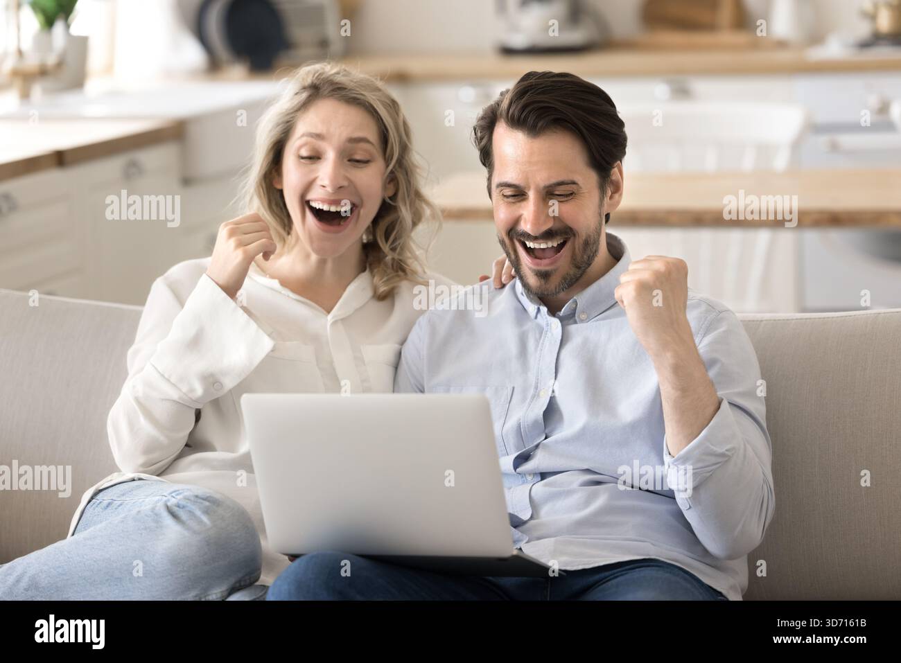 Felicissima coppia di famiglie sorprese alzano i pugni guardando lo schermo di un notebook Foto Stock