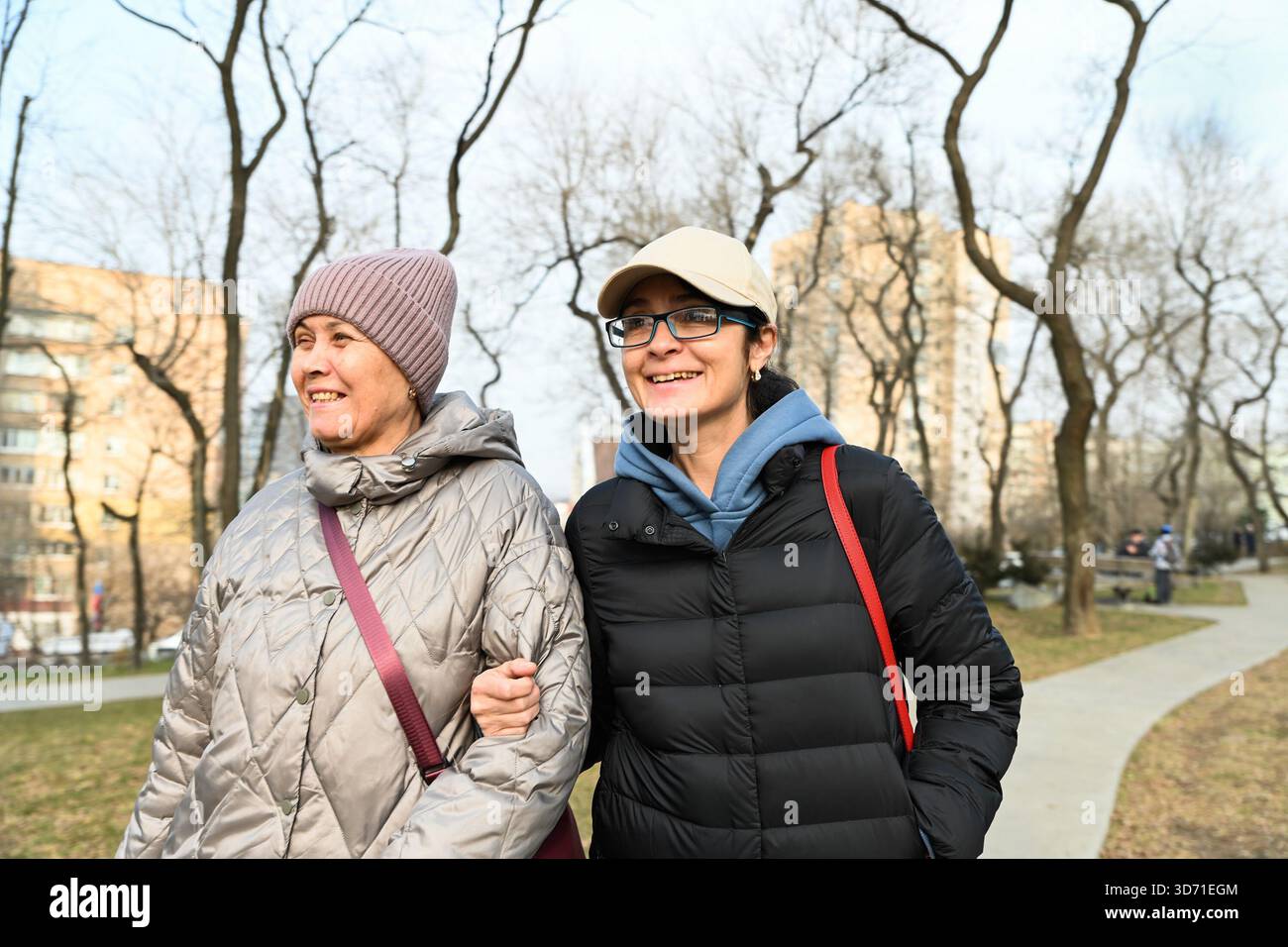 Una donna russa di 50 anni e il suo amico di 60 anni camminano braccio nel braccio in un parco in primavera e ridono insieme. Foto Stock
