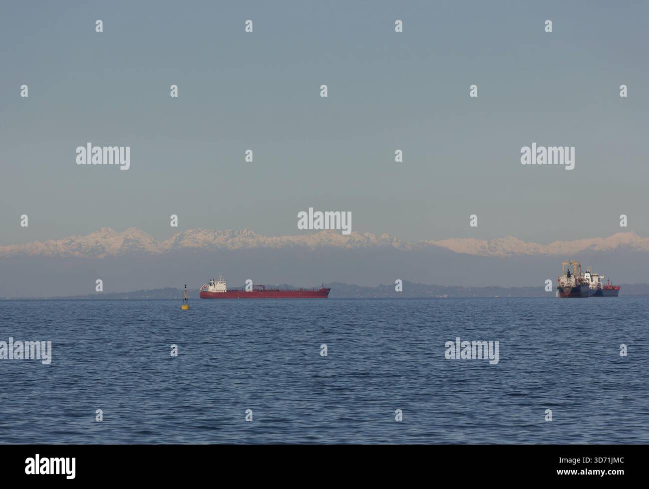 Nave da carico che naviga sul mare calmo con lontane montagne innevate all'orizzonte Foto Stock