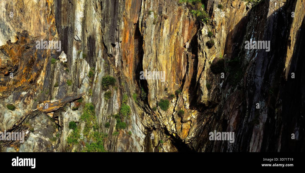 La luce del sole bacia un'aspra parete rocciosa, mettendo in evidenza le sue intricate crepe e fessure. Uno studio sulla luce, l'ombra e il passare del tempo. Foto Stock