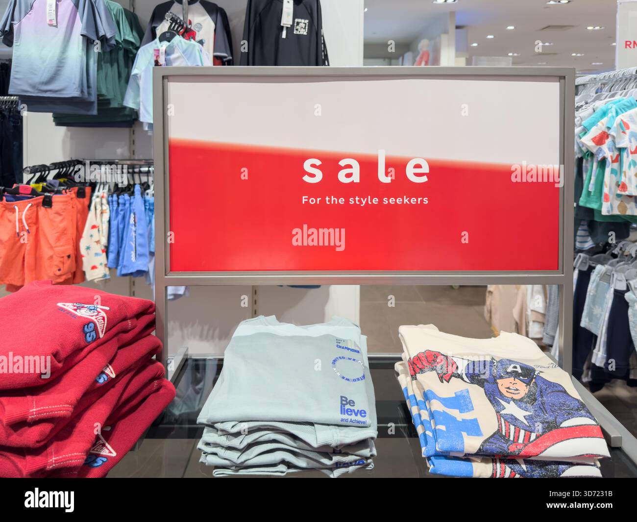 Penang, Malesia - 24 giugno 2025: Mostra un cartello rosso che legge la vendita insieme a capi di abbigliamento piegati come camicie e pantaloncini in vari modi Foto Stock