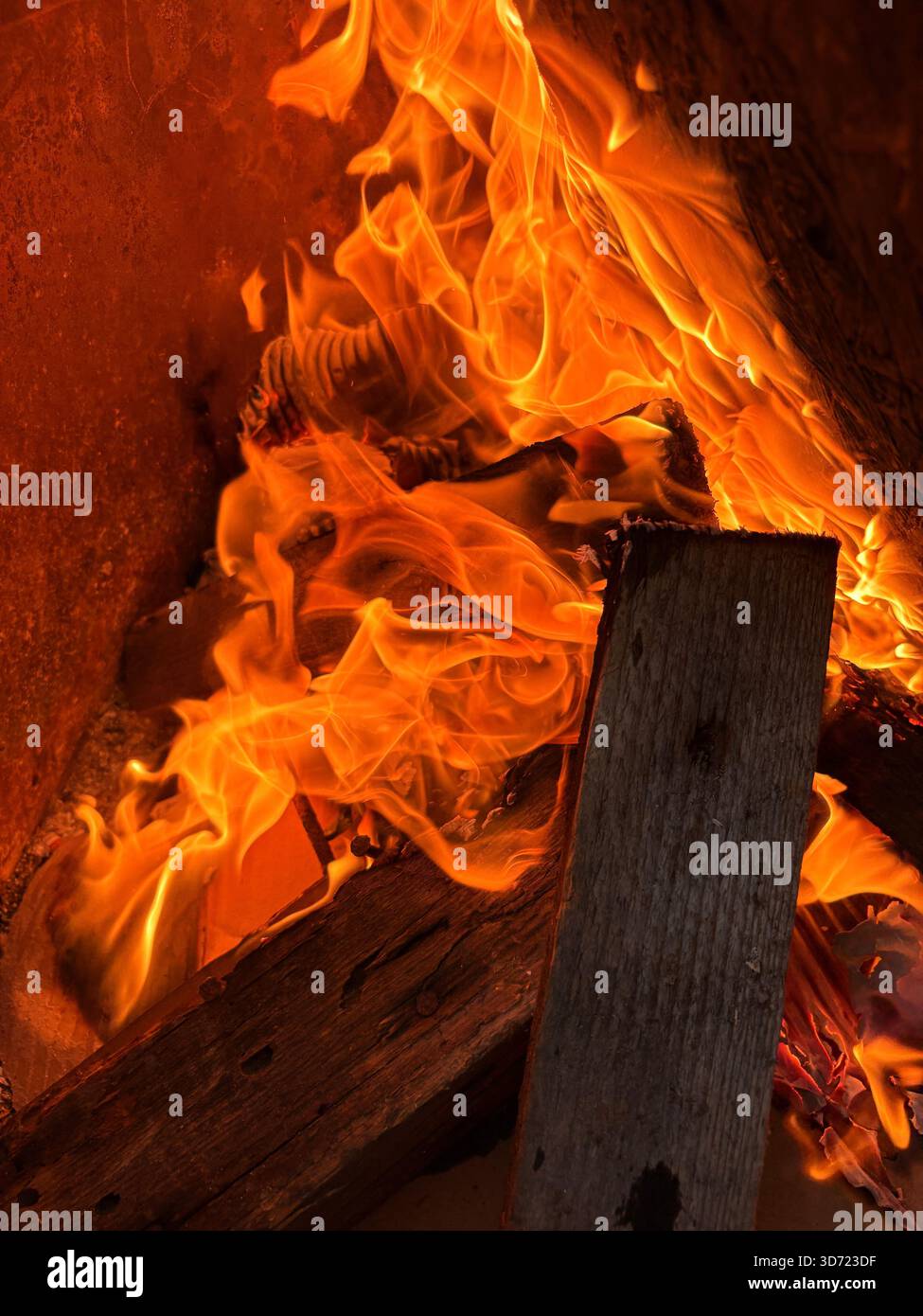 Primo piano di fiamme vivide che consumano tavole di legno, con sfumature arancioni e gialle che ruotano intorno al legno testurizzato. L'immagine acquisisce gli intensi Foto Stock