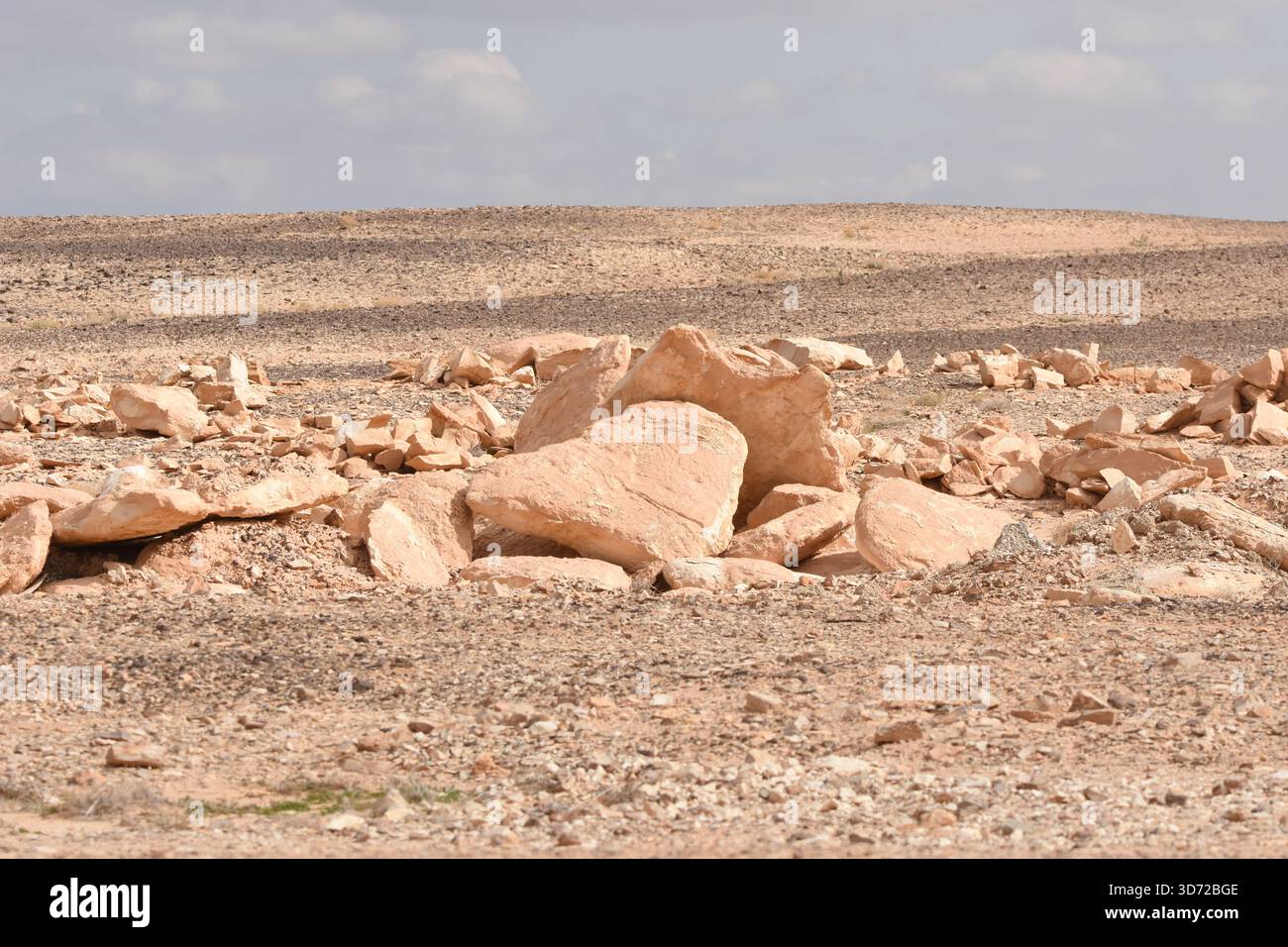 Un paesaggio arido presenta rocce e pietre sparse, rivelando modelli di erosione sulla superficie terrestre sotto un cielo blu limpido. Il terreno secco e roccioso Foto Stock