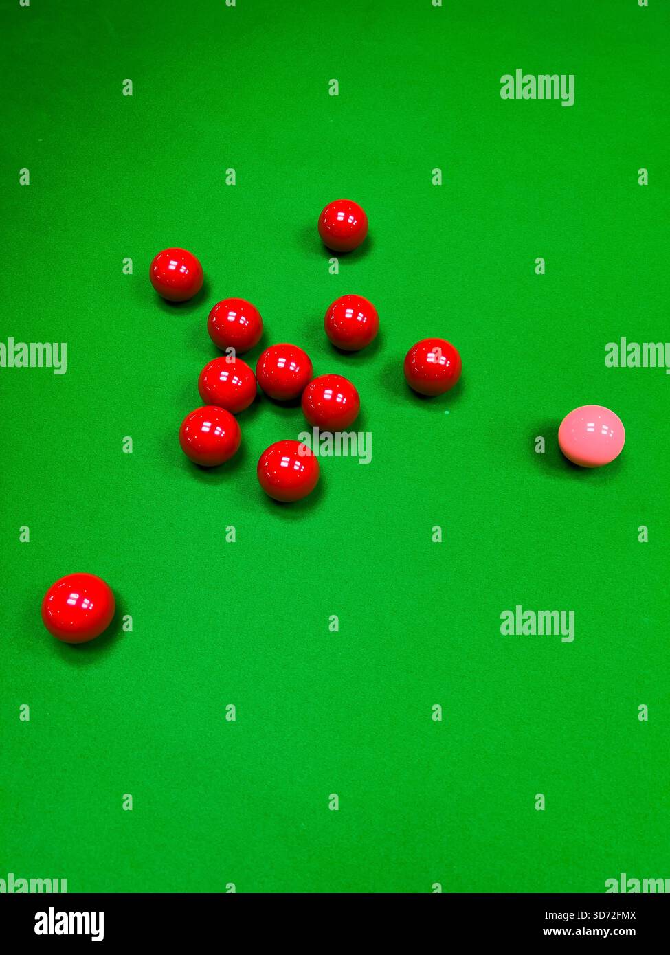 Una vista ravvicinata e ad angolo alto di diverse palle rosse da snooker e una palla rosa sparse sul feltro verde brillante di un tavolo da biliardo. Foto Stock