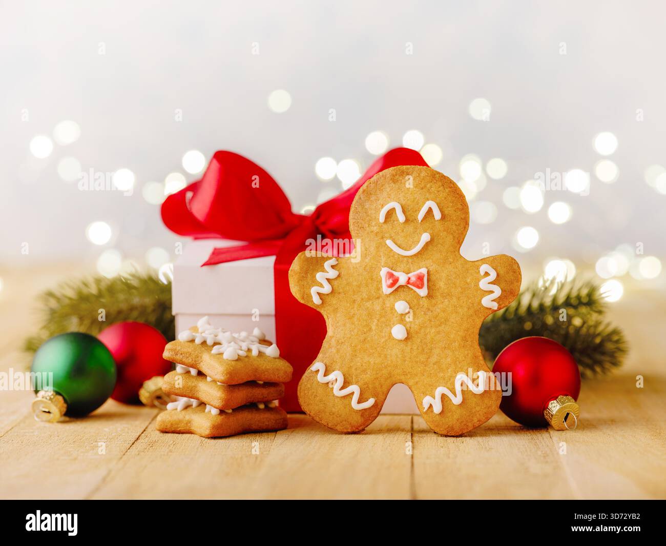 Biscotti di pan di zenzero natalizio con decorazioni natalizie, rami di alberi di Natale, regali e giocattoli su sfondo in legno con ghirlanda bokeh. Elemento di design del biglietto di Natale. Foto Stock