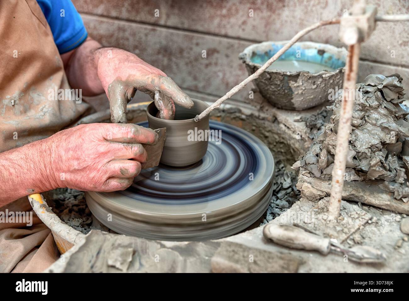 Primo piano di mani che modellano l'argilla su una ruota di ceramica rotante durante la lavorazione tradizionale della ceramica, mostrando il processo creativo, la consistenza dell'argilla bagnata e l'arte Foto Stock