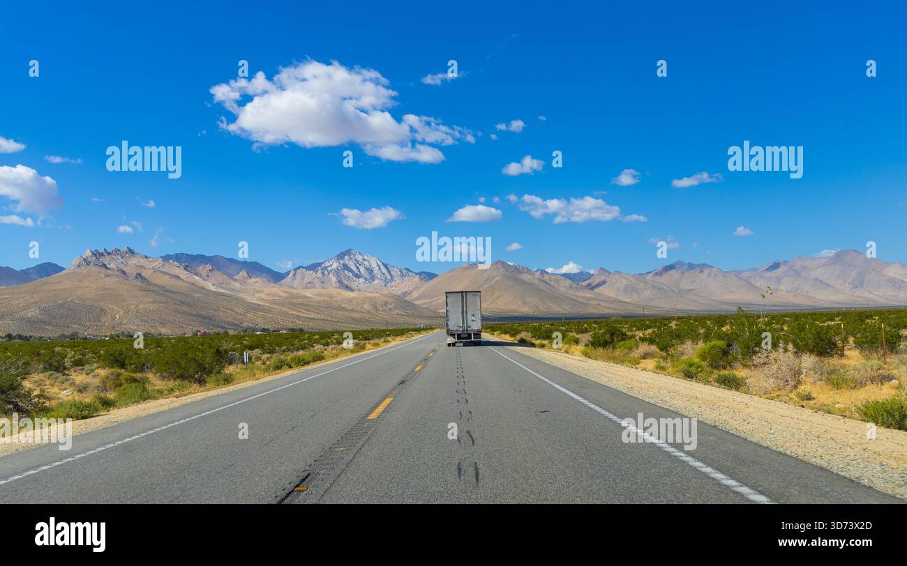 La desolata autostrada US Route 395 che si estende verso l'orizzonte nella regione della Sierra orientale della California. In lontananza c'è un camion abbandonato. Foto Stock