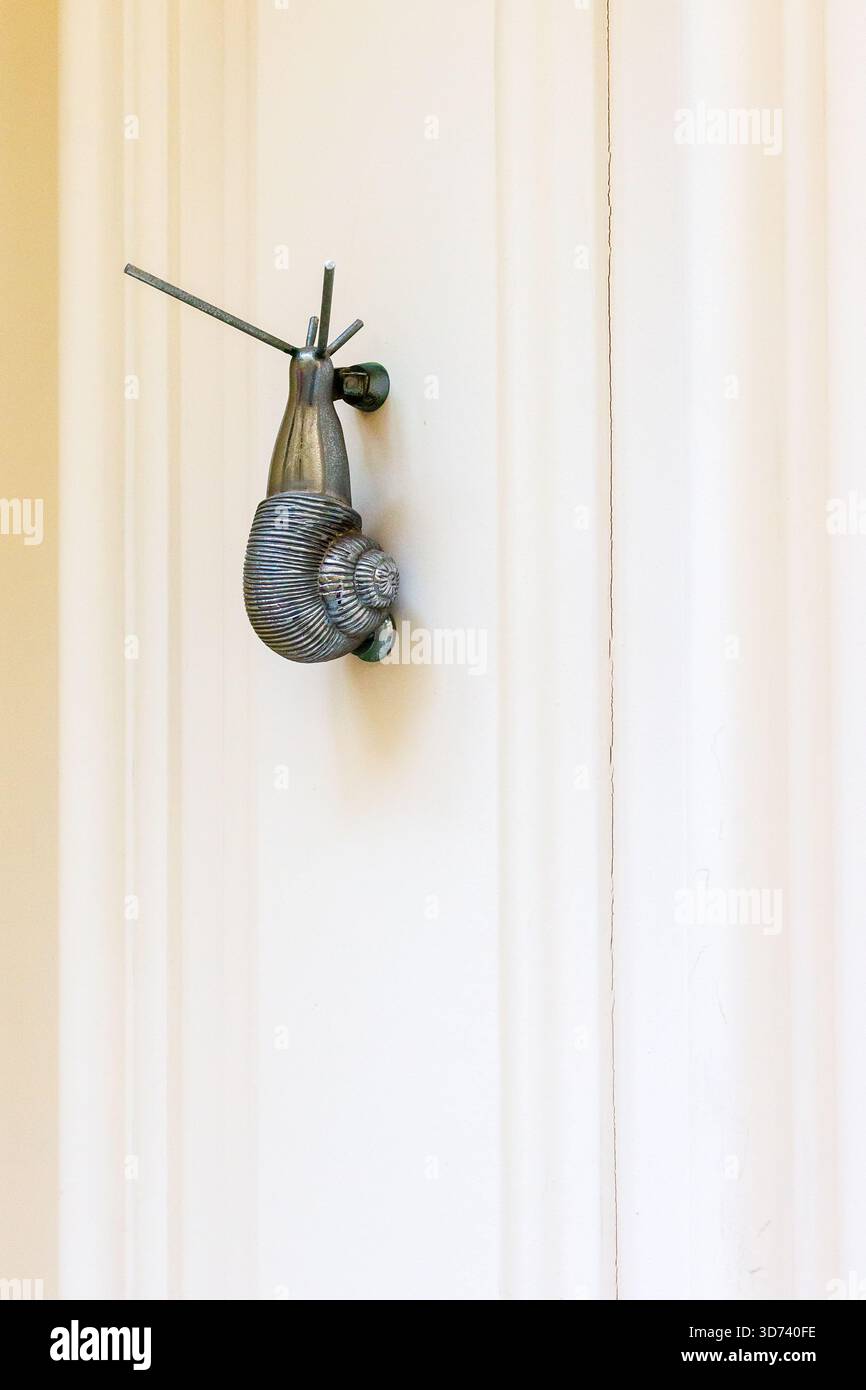 Maniglia per porta in metallo vintage a lumaca montata su una porta rivestita di pannelli bianchi, dettagli in metallo decorati Foto Stock