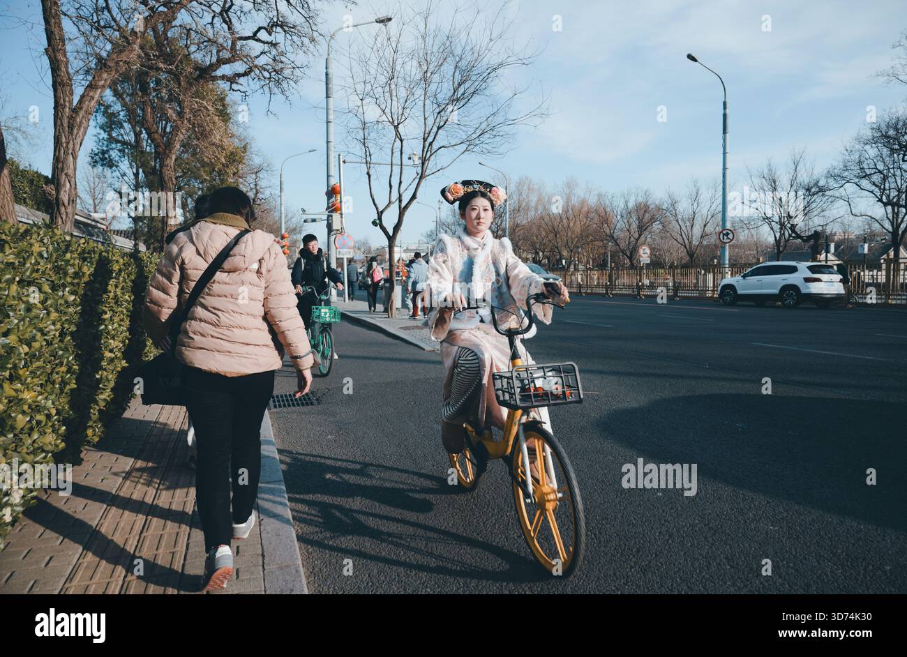 Il ciclista di Hanfu su una bicicletta gialla percorre un viale a Pechino, l'eleganza del vecchio mondo e la vita moderna della città Foto Stock