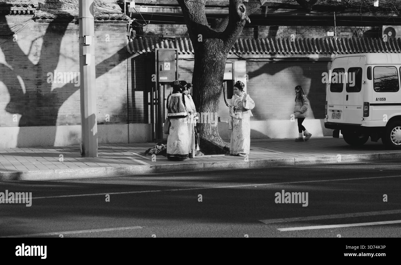 Gli amici vestiti di Hanfu chiacchierano accanto a un albero su un marciapiede invernale a pechino Foto Stock