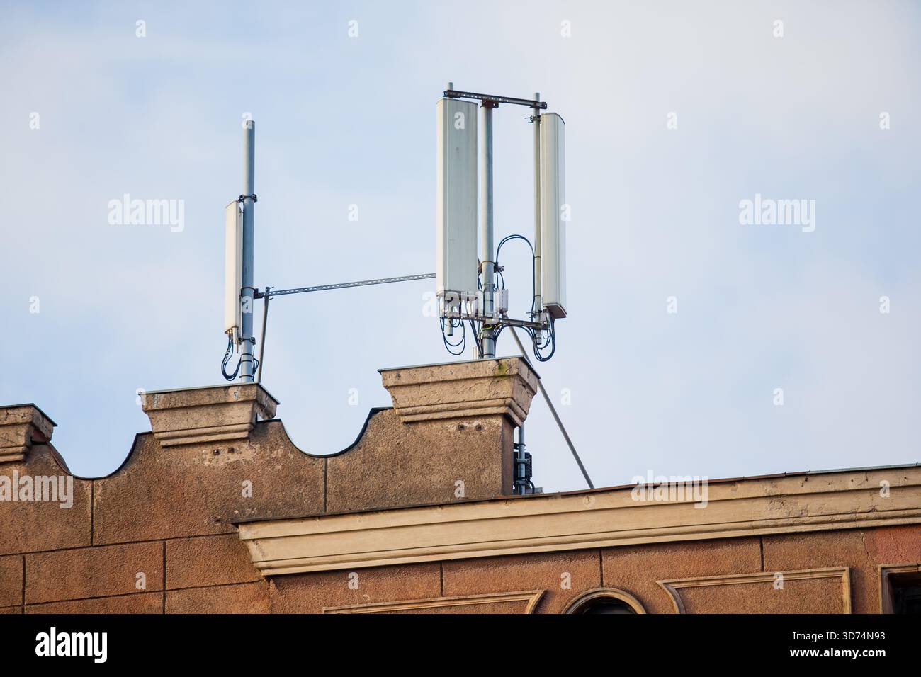 Cluster di apparecchiature di comunicazione cellulare con antenne a pannello, supporti per cablaggio e telai in metallo posizionati sul tetto con facciate di edifici testurizzate Foto Stock