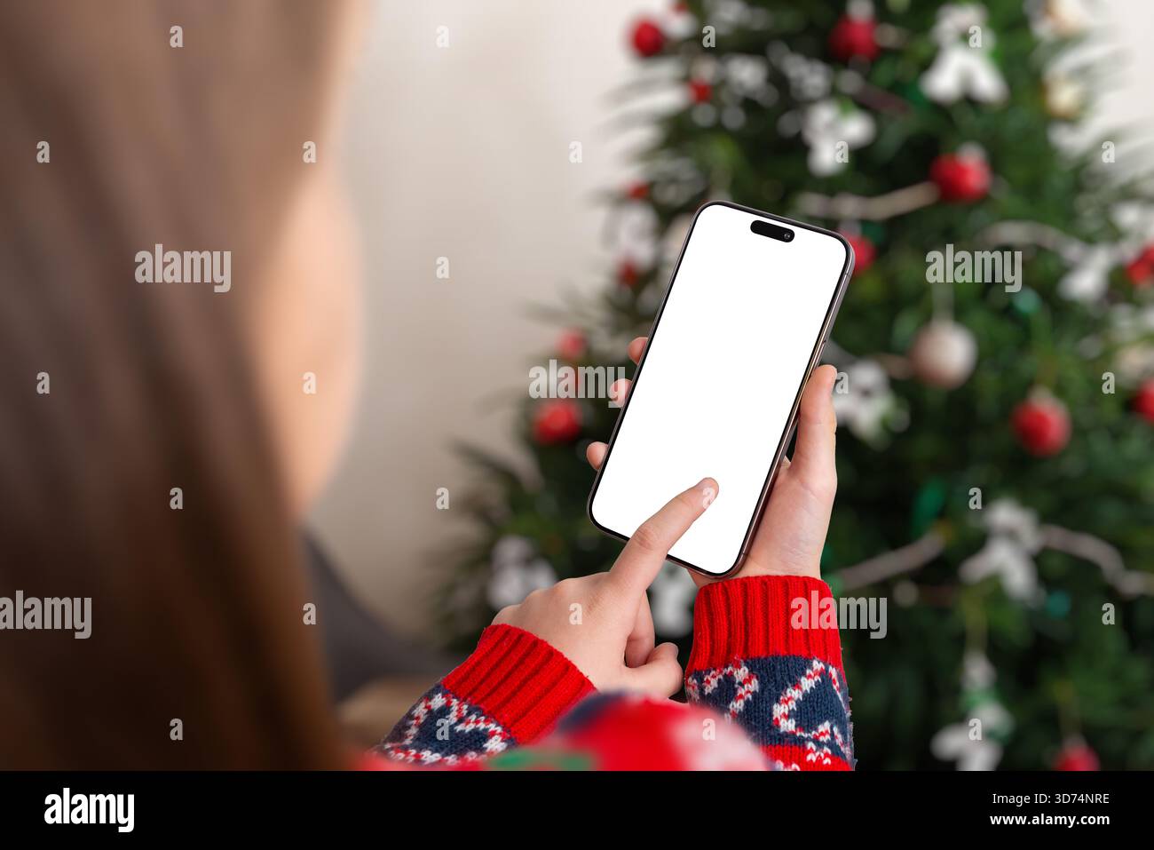 Ragazza che tiene in mano uno smartphone con schermo vuoto vicino all'albero di Natale, perfetta per i mockup delle app per le vacanze, la pubblicità stagionale, le promozioni mobili e le festività Foto Stock