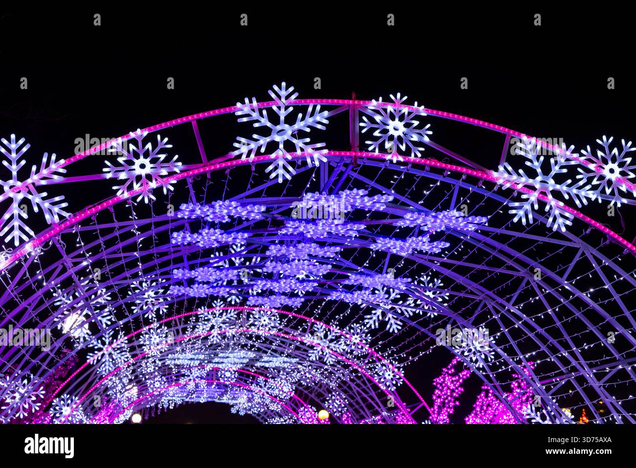 Tunnel ad arco decorato con luci brillanti fiocchi di neve che creano un'esperienza di vacanza invernale coinvolgente di notte Foto Stock